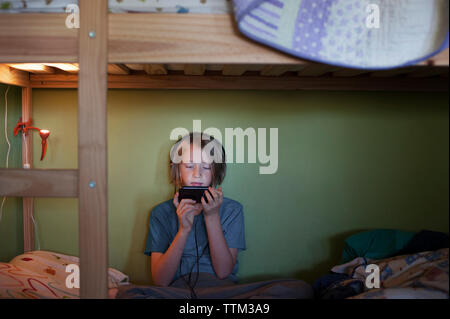 Boy using smart phone while sitting on bunkbed Stock Photo