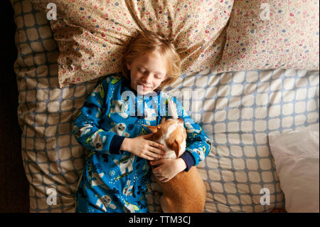 Overhead shot of smiling boy sleeping with dog on bed Stock Photo