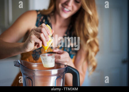 Woman squeezing lemon in cup over jar Stock Photo