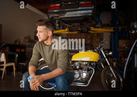 Man looking away while sitting on stool in garage Stock Photo