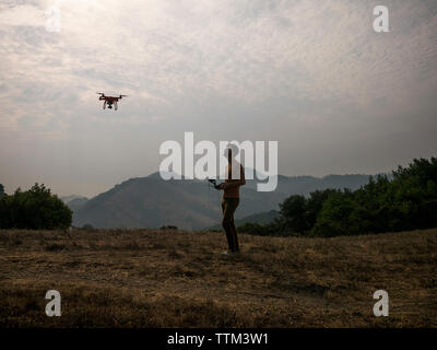 Side view of man operating drone through remote control against mountains Stock Photo