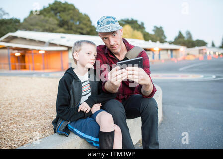 Father and son talking selfie through mobile phone while sitting on street Stock Photo