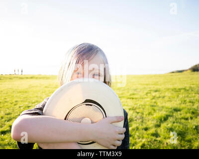 Portrait of boy holding hat while standing on grassy field against sky Stock Photo