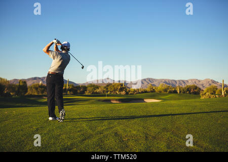 Rear view of man playing golf against clear blue sky Stock Photo