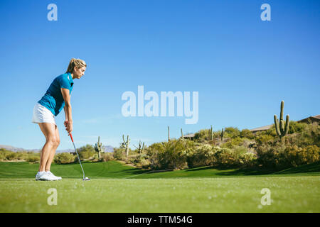 Side view of woman playing golf on field against blue sky Stock Photo