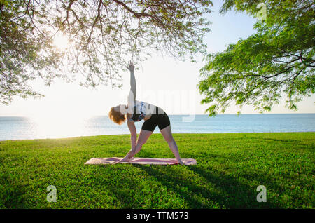 Woman practicing yoga at park against sea and clear sky Stock Photo