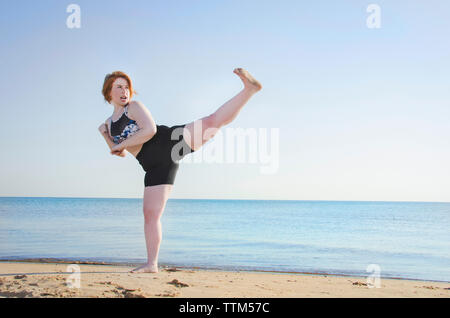 Woman practicing kickboxing at beach against clear sky Stock Photo