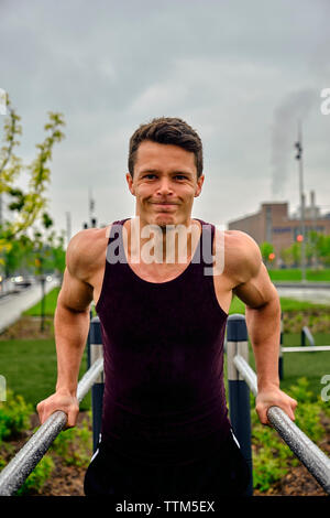 Portrait of young man doing dips on parallel bars at park in city Stock Photo