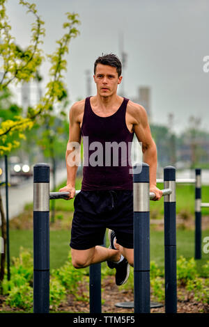 Full length of young man doing dips on parallel bars at park in city Stock Photo