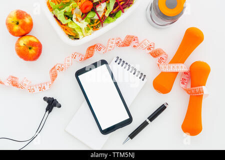 Fitness healthy and dieting plan mockup on tablet with blank screen mobile phone for mockup, earphone, bottle of water, salad, apples and measuring ta Stock Photo