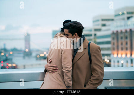 Couple in warm clothing embracing while standing in balcony Stock Photo