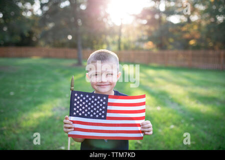 Portrait of smiling boy holding American flag while standing on field in yard Stock Photo
