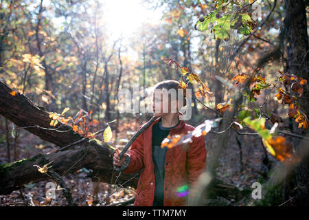 Boy holding stick while standing in forest during autumn Stock Photo