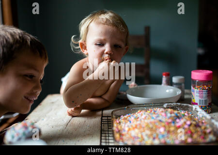 Toddler girl looking at brother while sneaking sprinkles off of a cake Stock Photo