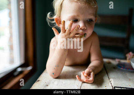 Toddler girl licking sticky messy fingers covered in colorful sprinkle Stock Photo