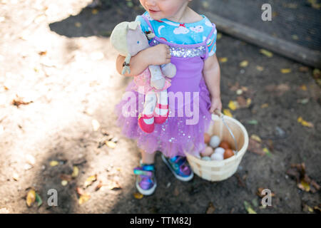 Happy toddler girl with baby doll dressed up with basket of eggs Stock Photo