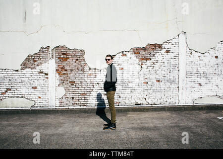 Side view of young man standing against damaged wall Stock Photo
