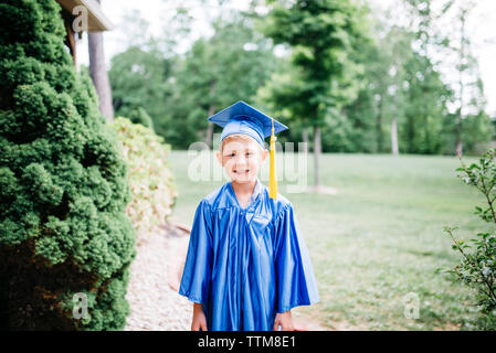 Portrait of happy boy in graduation gown standing at park Stock Photo