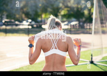 Rear view of sporty woman holding towel around neck on field Stock Photo