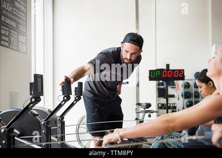 Instructor checking rowing machine while women exercising in crossfit gym Stock Photo