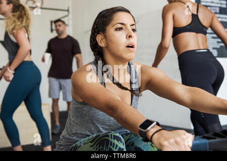 Woman exercising on rowing machine against athletes in crossfit gym Stock Photo