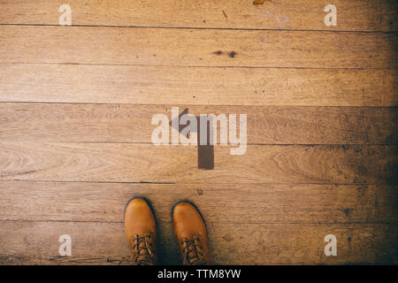 Low section of woman wearing shoes while standing by arrow symbol on wooden floor Stock Photo