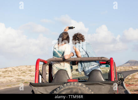 Two surfer girls  on a 4x4 jeep taking selfie Stock Photo