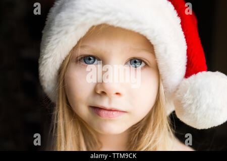 Portrait of cute girl in Santa hat against black background Stock Photo