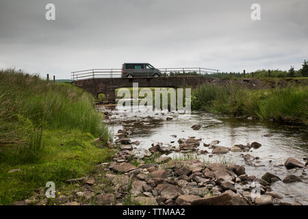 Motor home moving on bridge over river against cloudy sky Stock Photo