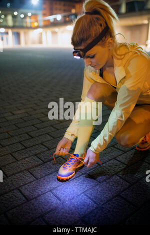 Female athlete tying shoelace on footpath at night Stock Photo