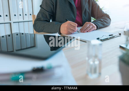 Businesswoman signing contract agreement, reflection on tablet computer placed on office desk Stock Photo