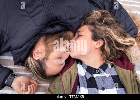 Overhead view of couple kissing while lying on blanket Stock Photo