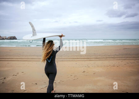 Woman carrying surfboard while walking on beach against sky Stock Photo