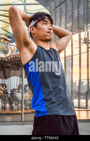 fit young man stopsand stretches after running workout near carousel in Brooklyn Bridge Park at dusk Stock Photo