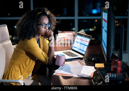 Thoughtful businesswoman holding coffee cup while sitting on chair in office at night Stock Photo