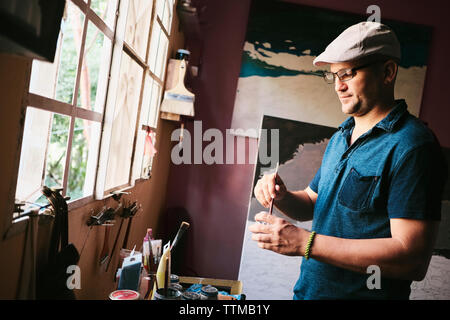 Mid adult male Cuban artist mixing paint with brush in his workshop Stock Photo