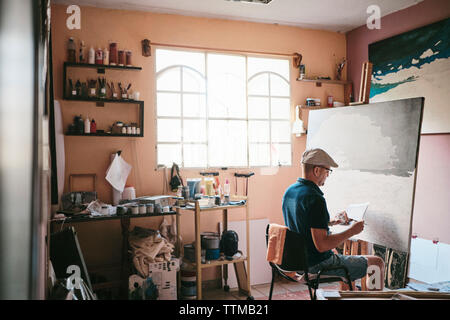 Mid adult man working as painter with brush and canvas in his studio