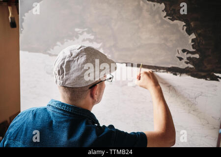 Mid adult Cuban artist painting with brush on canvas in his studio Stock Photo