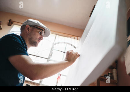 Mid adult Cuban artist painting with brush on canvas in his studio