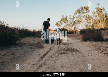 Rear view of siblings walking on ground against sky Stock Photo