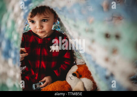 Boy playing with toys while sitting under blanket in bedroom Stock Photo