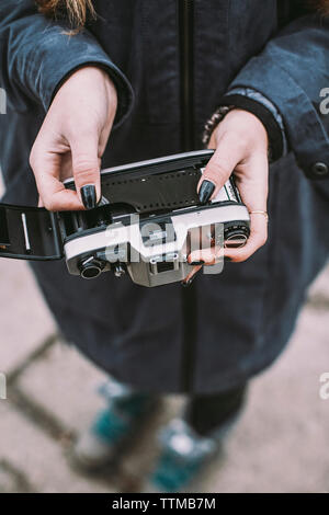 Low section of woman holding vintage camera with film negative while standing on footpath Stock Photo