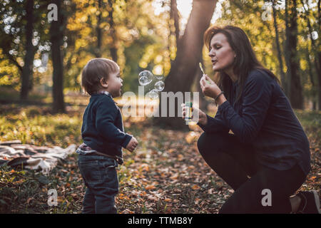 Mother and son playing with bubbles at park during autumn Stock Photo