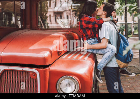 Side view of young couple kissing on mouth in city by vintage bus Stock Photo