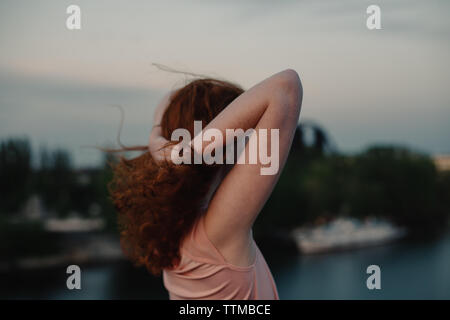 Side view of woman holding hair while standing on bridge at dusk Stock Photo