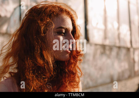 Side view portrait of young red haired woman standing in the sun