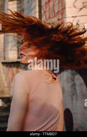 Redheaded teenager tossing hair while walking in city street Stock Photo
