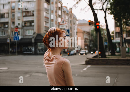 Young redheaded woman holding hair while standing in city street Stock Photo