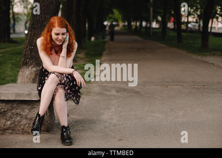 Young happy woman talking on mobile phone while sitting in park Stock Photo