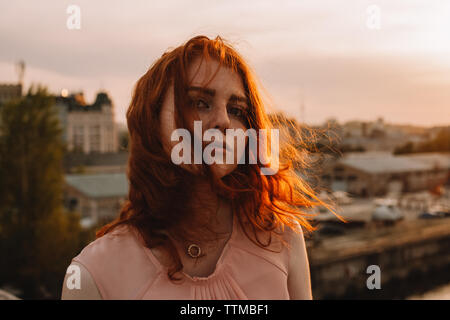 Portrait of young cute woman standing on bridge against city Stock Photo